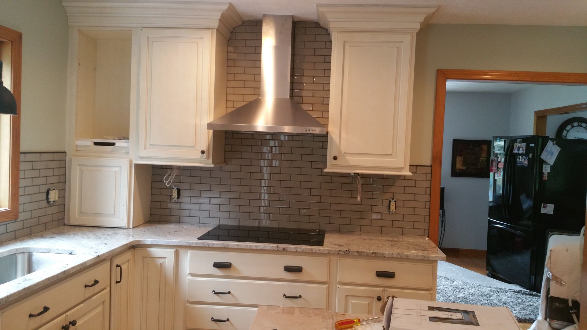 A kitchen with white cabinets, a stainless steel vent hood, and a gray brick backsplash above a dark countertop.