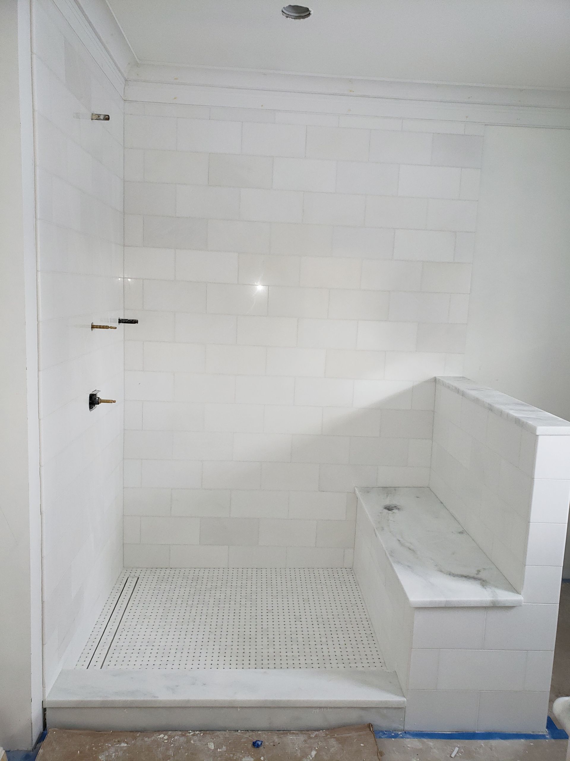 A walk-in shower with white tiled walls, a marble bench, a patterned tile floor, and a marble threshold.