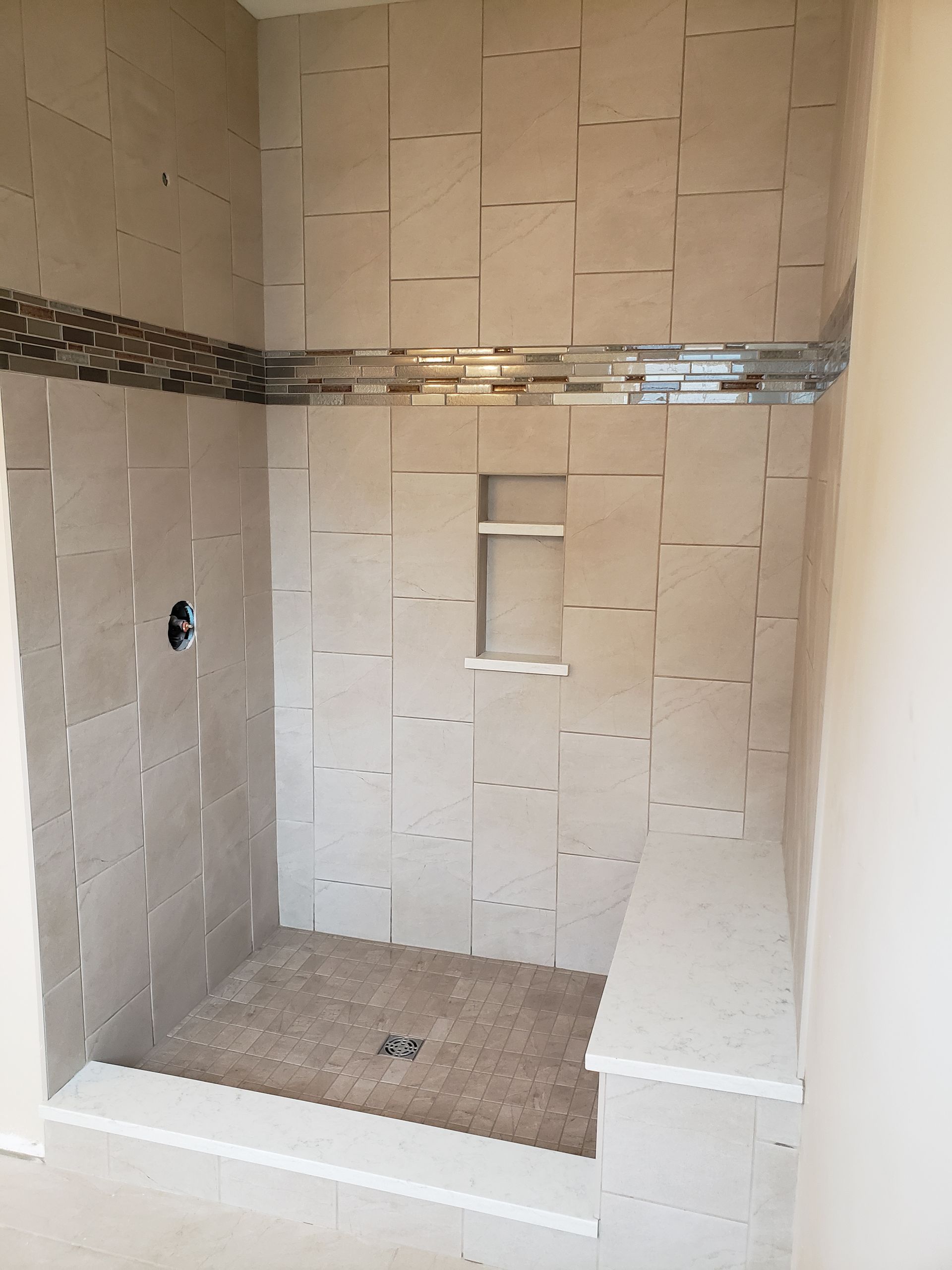 A tiled walk-in shower with a built-in bench, a recessed wall niche, and a decorative mosaic accent stripe.