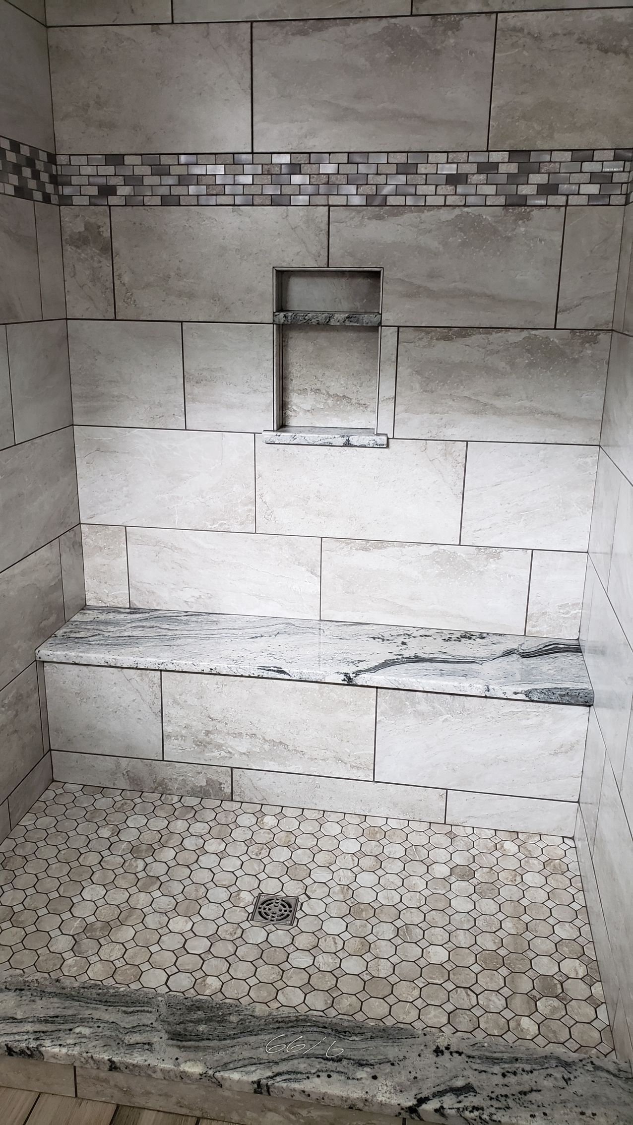 A shower under construction with beige wall tiles, a built-in bench, a small wall niche, and a pebbled shower floor.