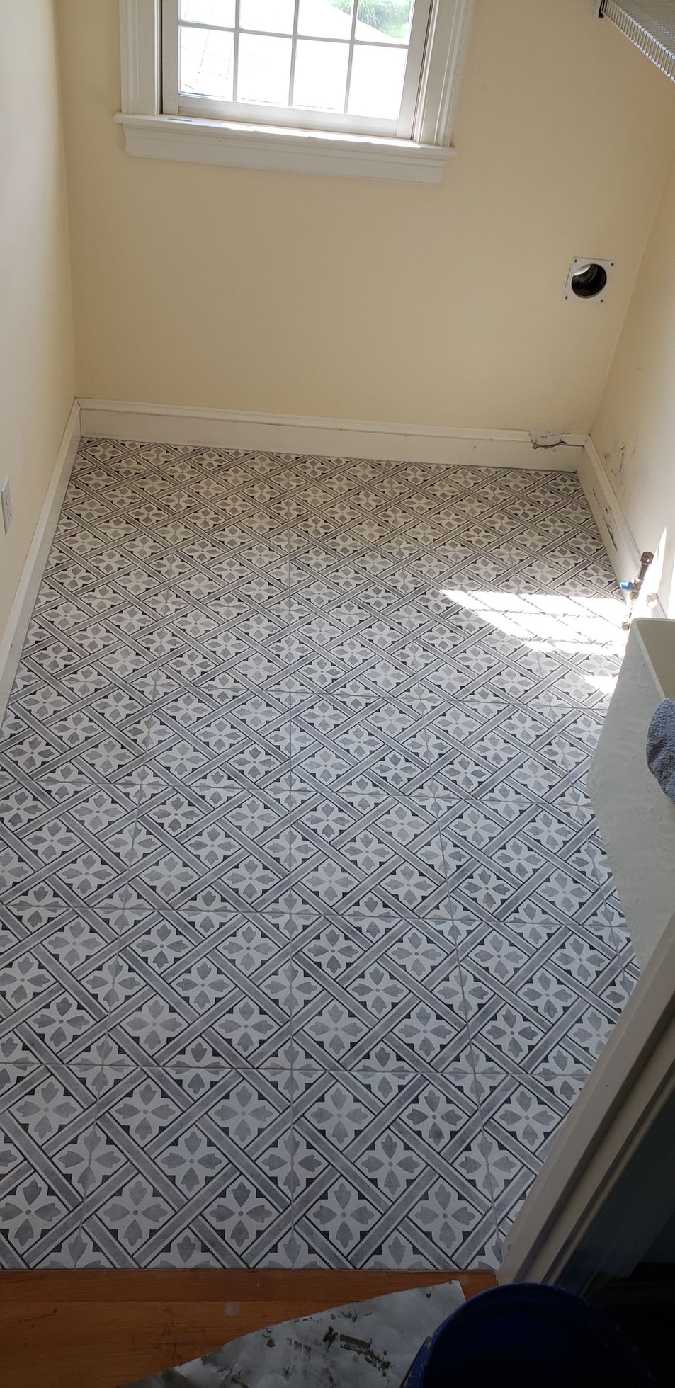 A small room featuring black and white patterned tile flooring beneath a window in a cream-colored wall.