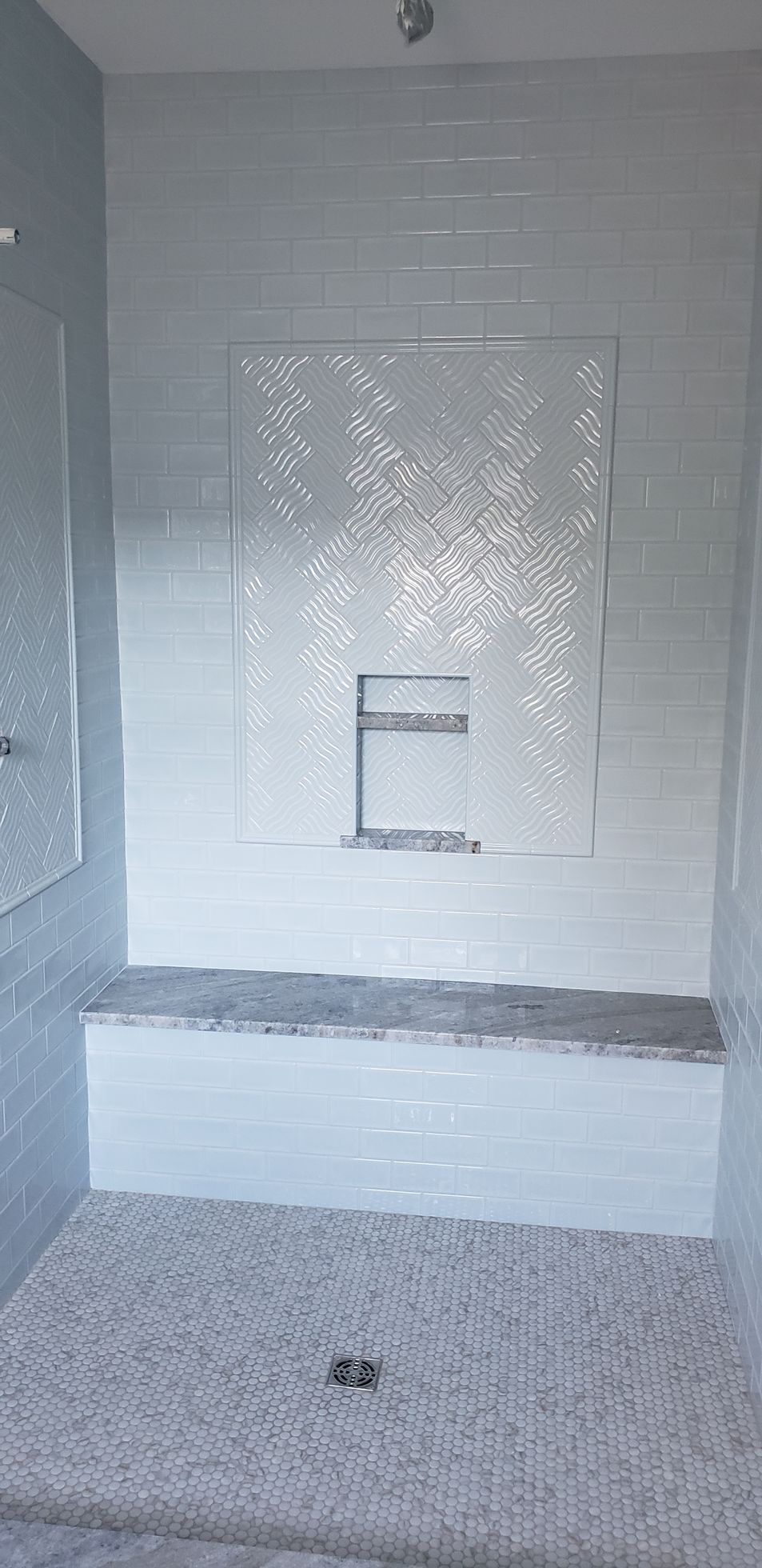 A modern tiled shower with a stone bench, a decorative mosaic feature wall, a built-in recessed niche, and a pebble floor.