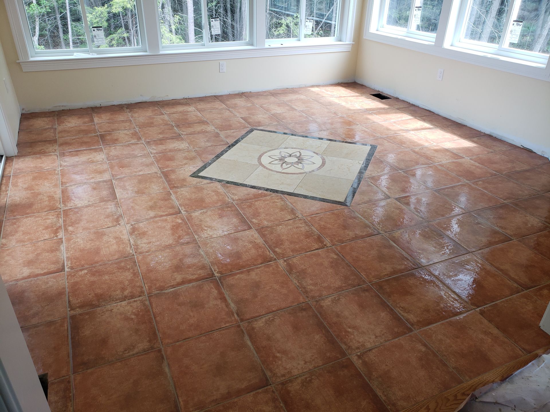 A sunroom floor with terracotta-colored tiles and a central decorative square inset with a circular pattern.