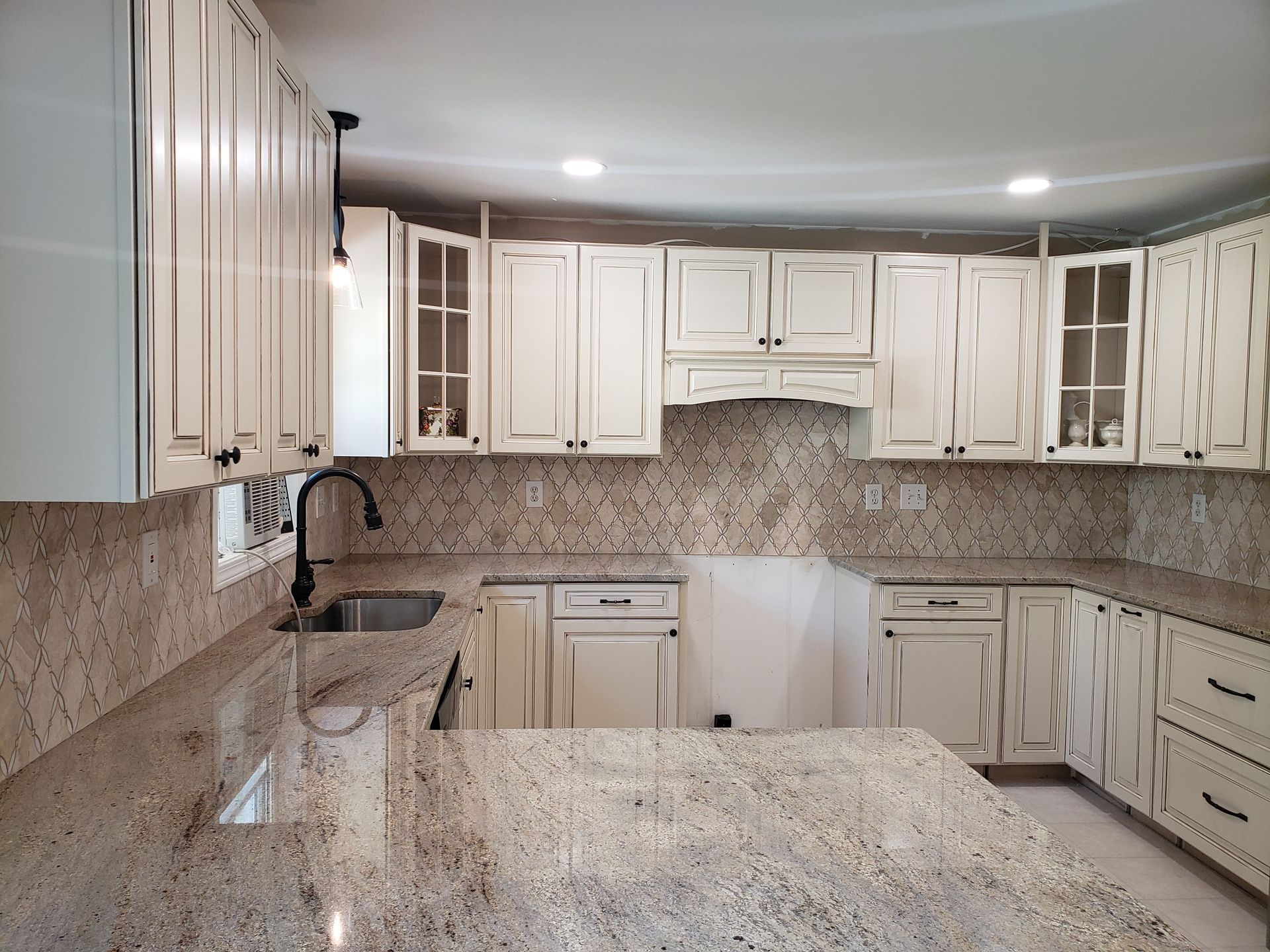 A bright kitchen featuring off-white raised-panel cabinets, granite countertops, patterned backsplash, and a sink.