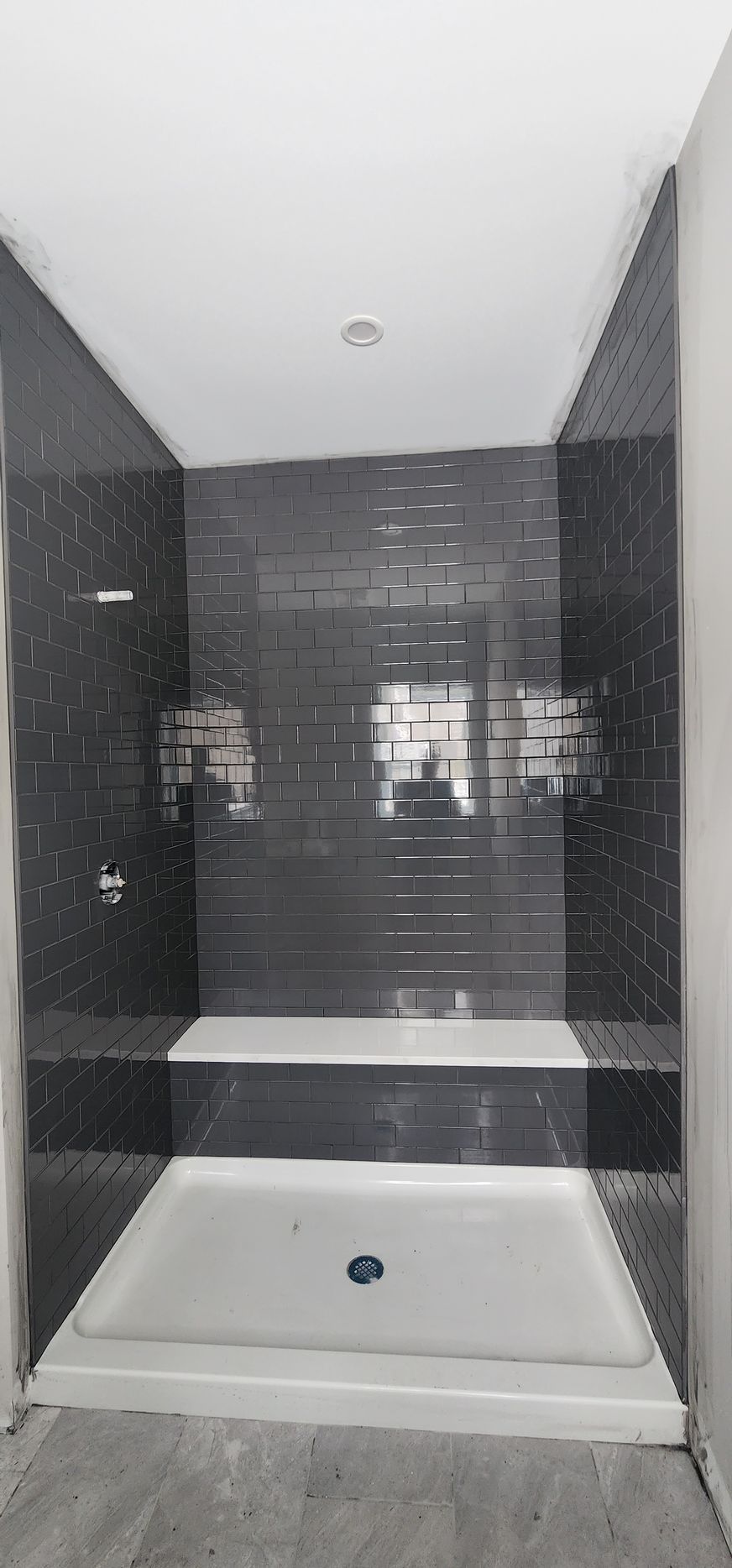 A shower stall with dark gray, horizontal tiled walls and a white floor and bench seat.
