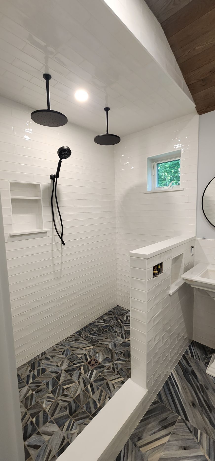 Modern walk-in shower with white tiled walls, black fixtures, and patterned dark grey stone flooring.