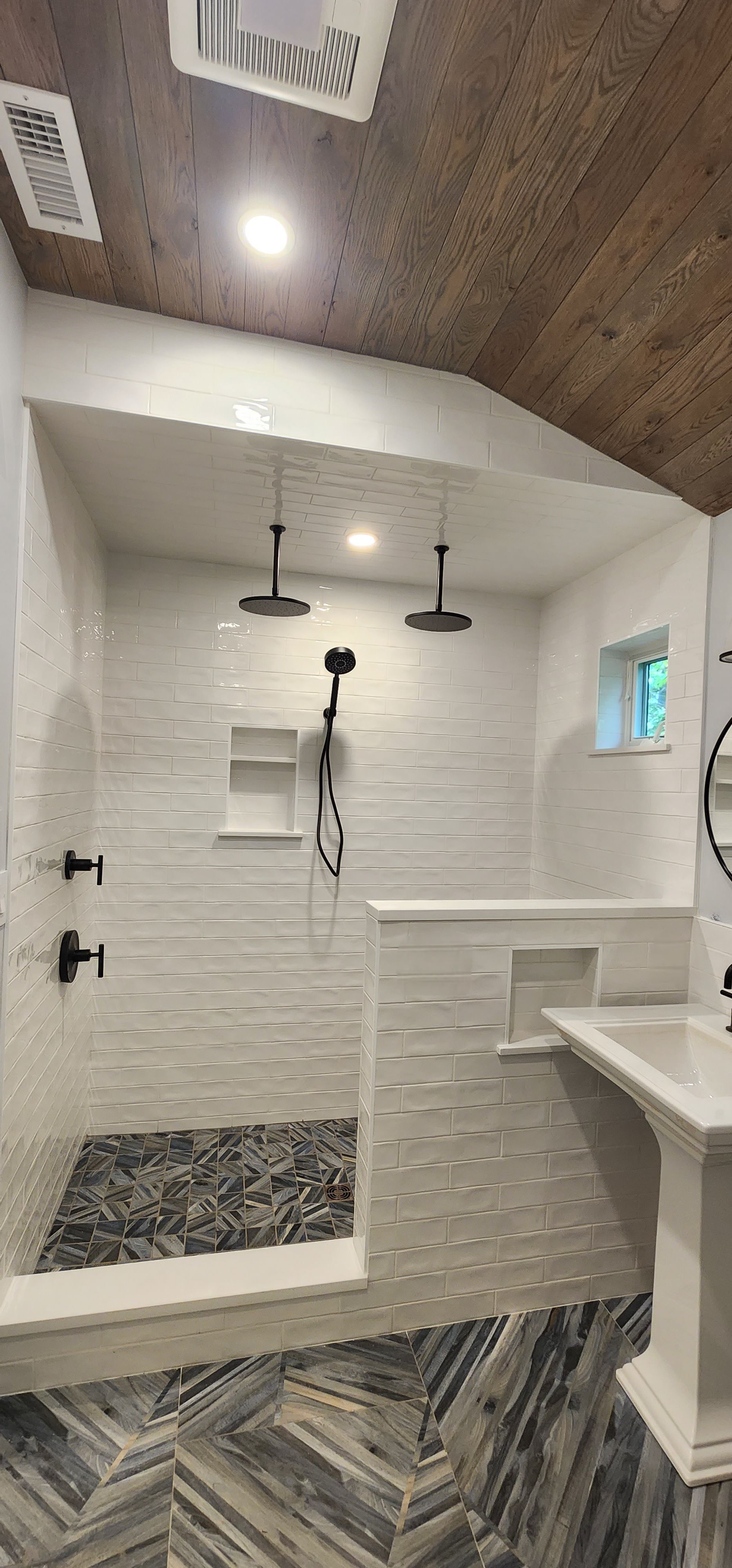 Modern bathroom with a tiled walk-in shower, dual rain showerheads, a handheld sprayer, and a dark stone floor.