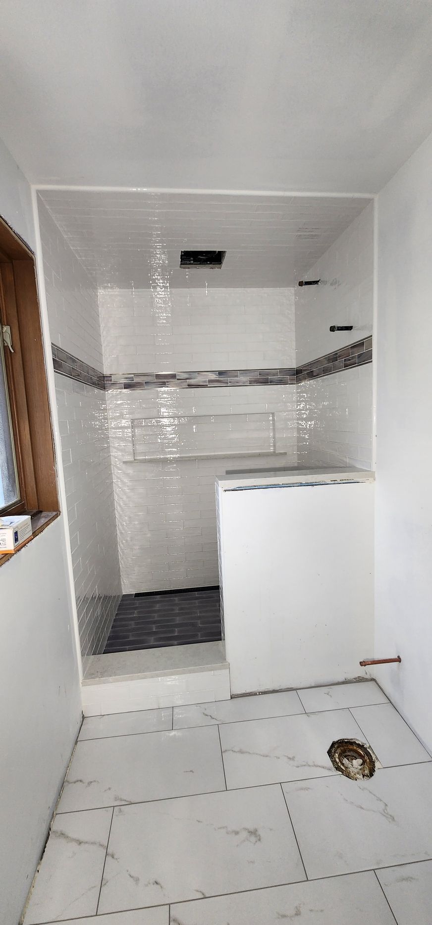 A bathroom renovation in progress featuring a tiled shower stall, a white half-wall, and white floor tiles.