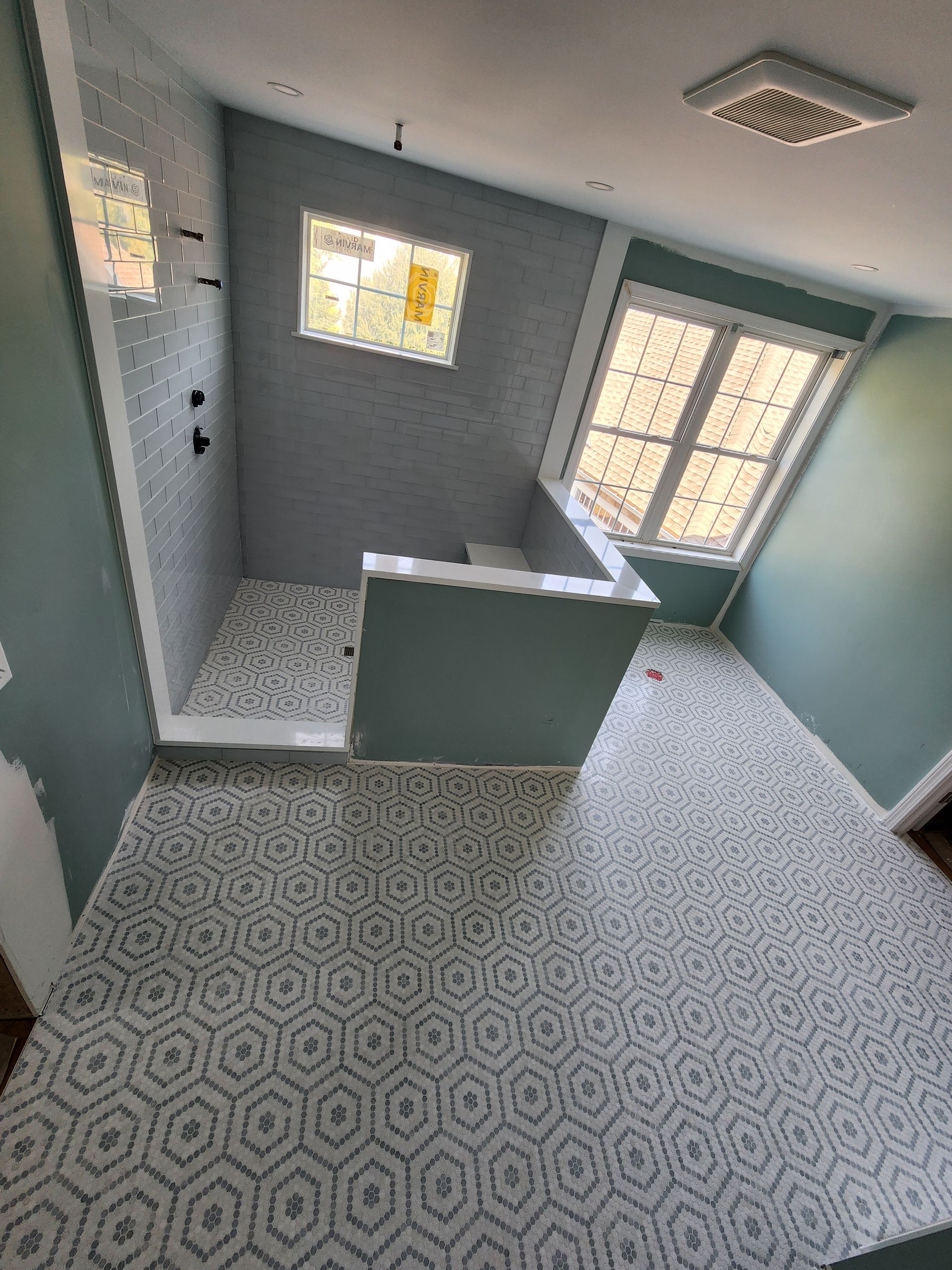 A bathroom under construction featuring geometric hexagonal floor tiles, light blue walls, and a walk-in shower enclosure.