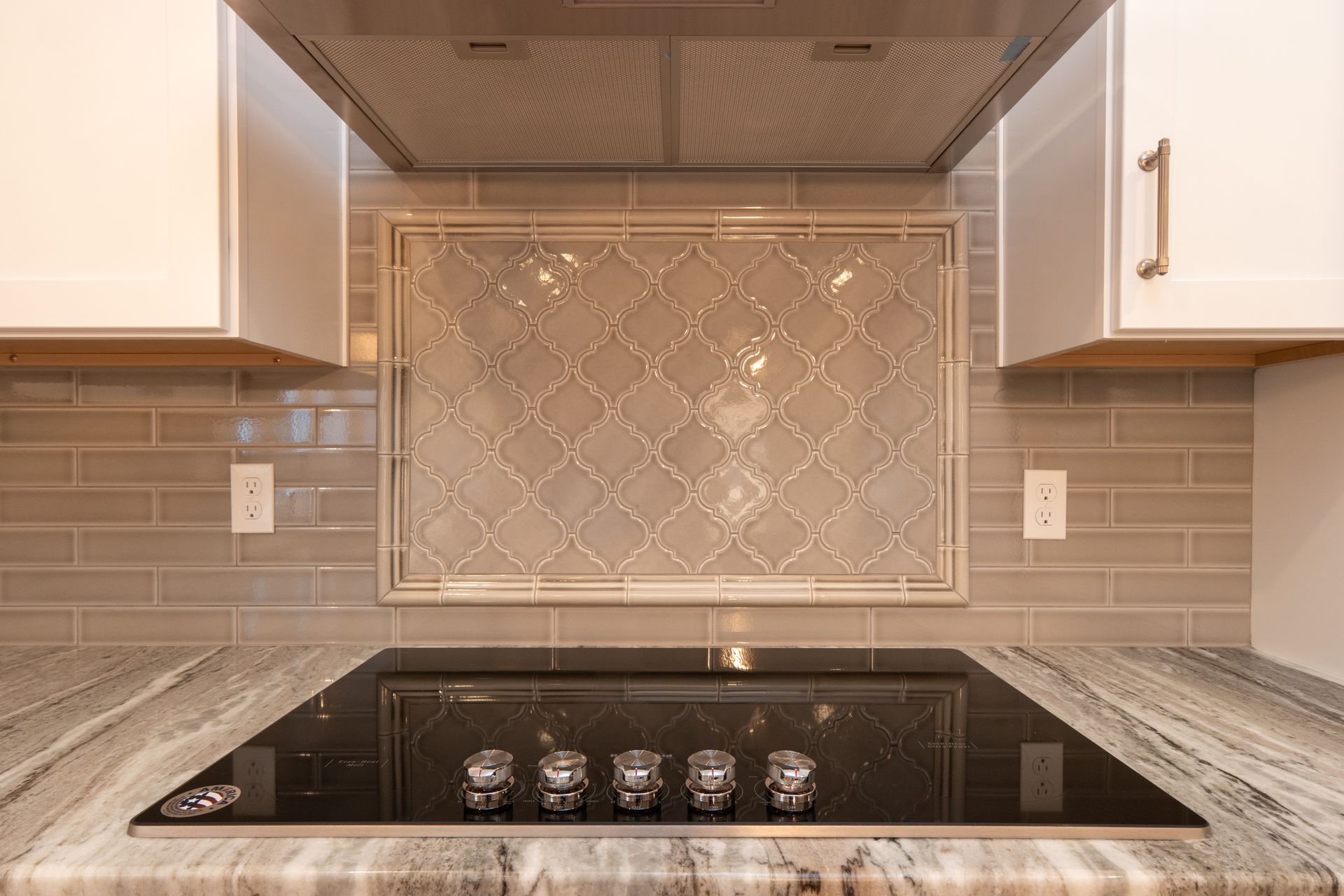 A modern kitchen stove with a black glass cooktop, stone countertop, and a decorative tile backsplash between cabinets.
