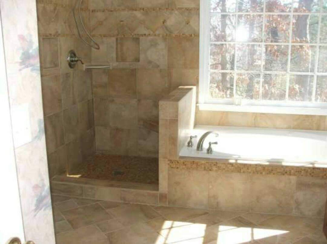 A bathroom with a tiled walk-in shower next to a bathtub under a large window with natural light.