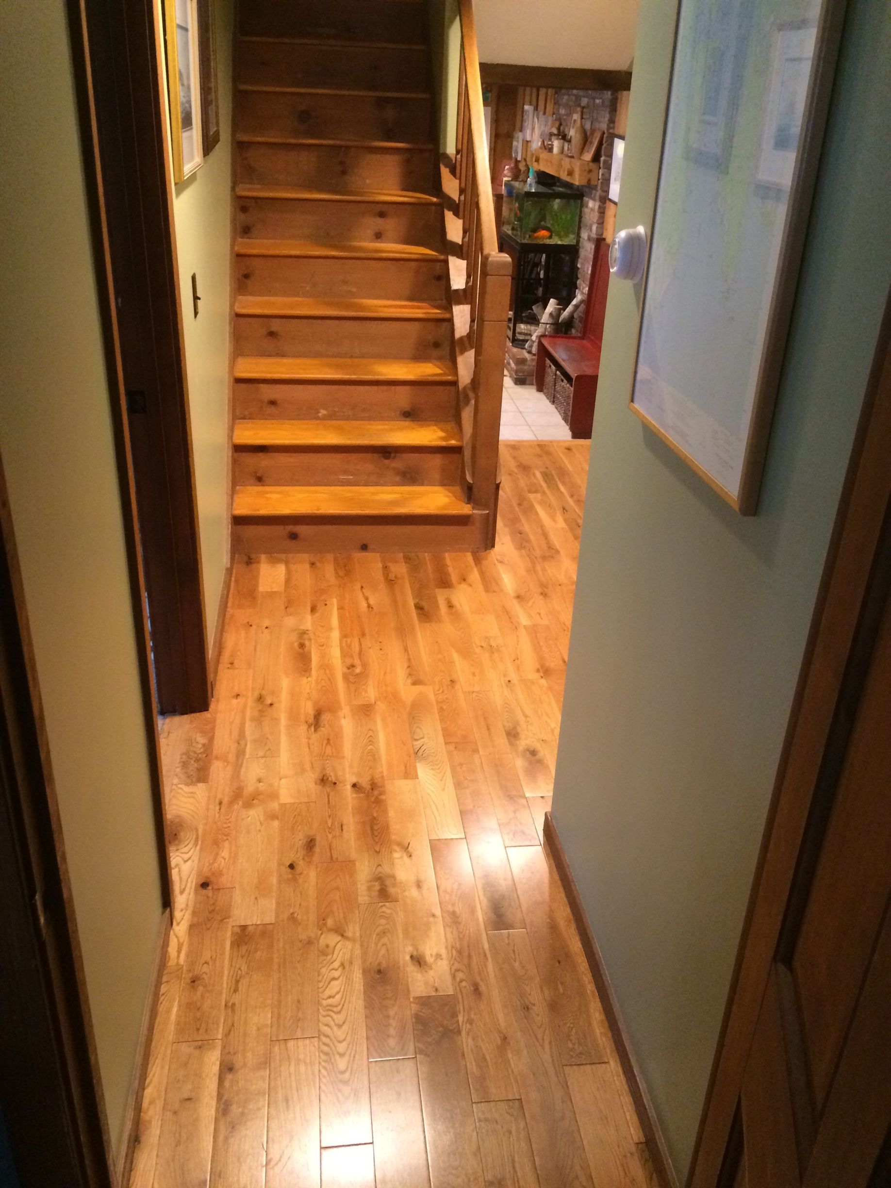 A hallway with light wood flooring leads to a wooden staircase, with light green walls on either side.