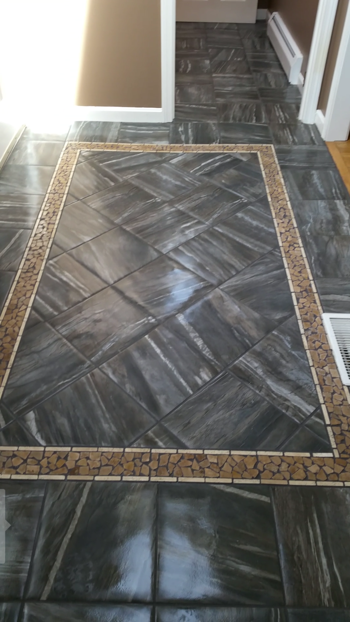 A black tile floor with a brown border in a hallway.