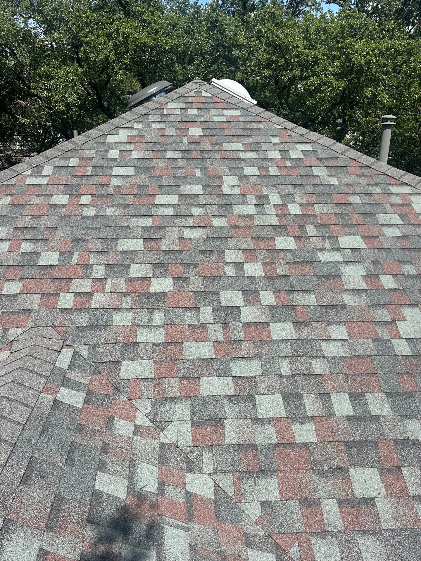 A close-up view of a shingled roof with a blend of grey, white, and reddish-brown tiles under bright sunlight.