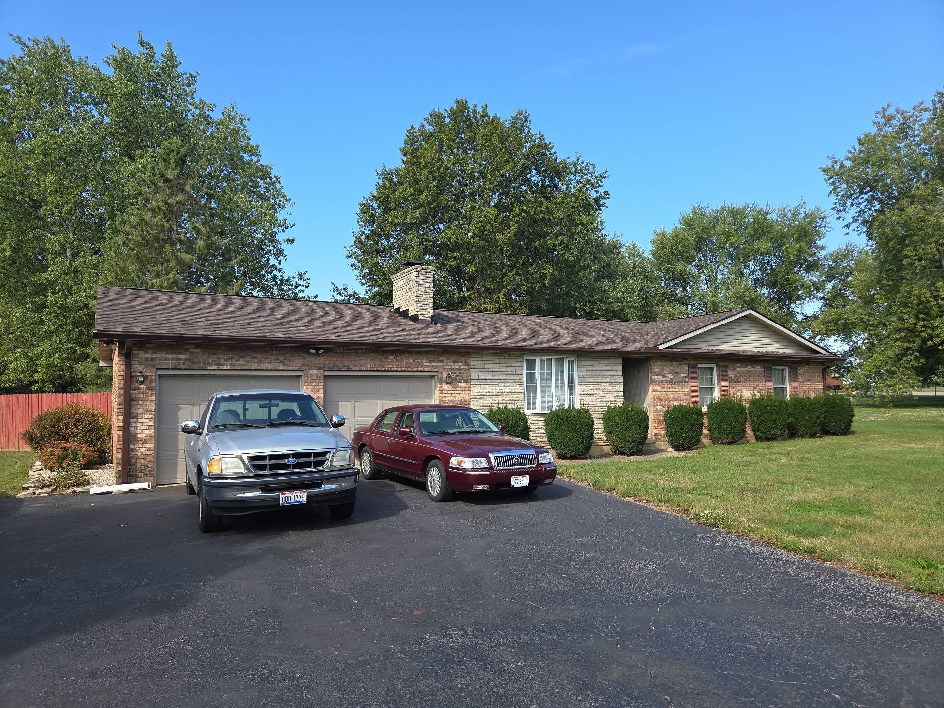 A single-story stone house with two garage doors and a long driveway parked with a silver pickup and a red sedan.