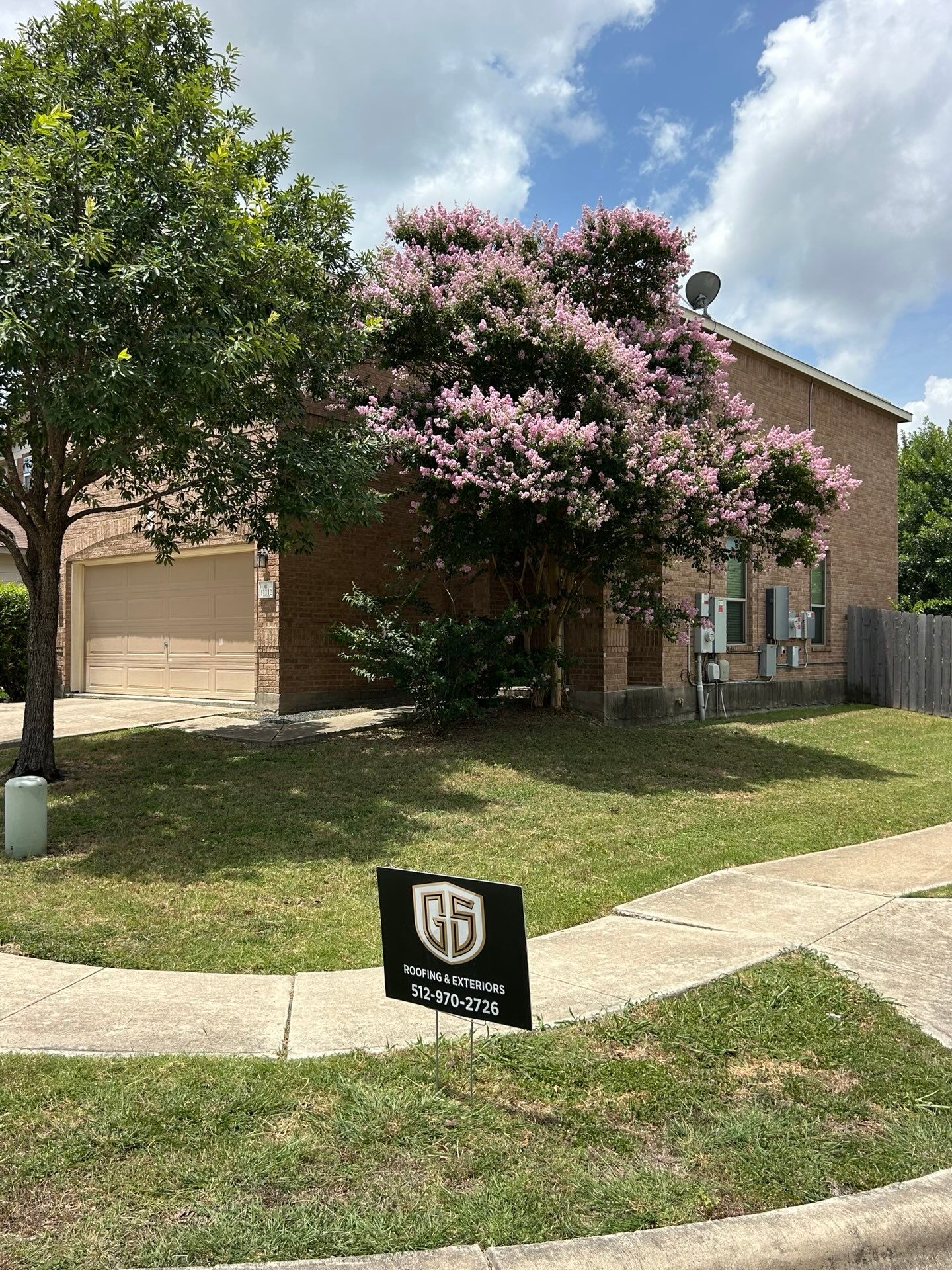 A beige brick house with a garage and a blooming crape myrtle tree, with a 