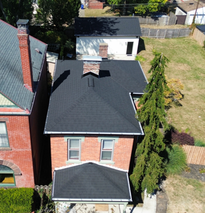 An aerial view of a brick house with a newly installed dark shingle roof, featuring a detached garage in the backyard.