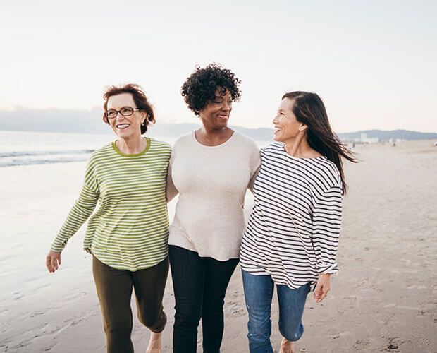 three women are walking on the beach together .