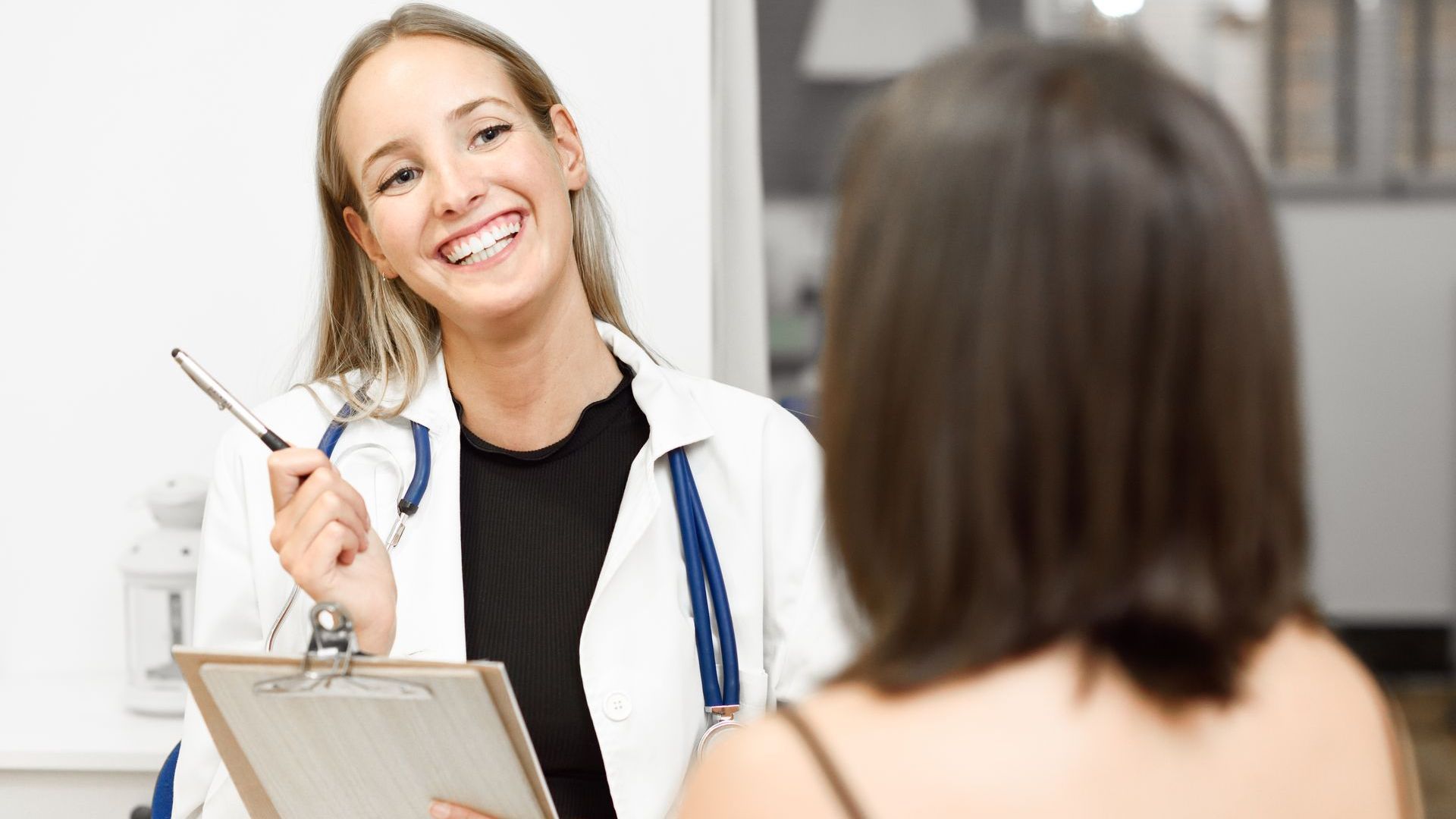 a female doctor is talking to a patient while holding a clipboard .