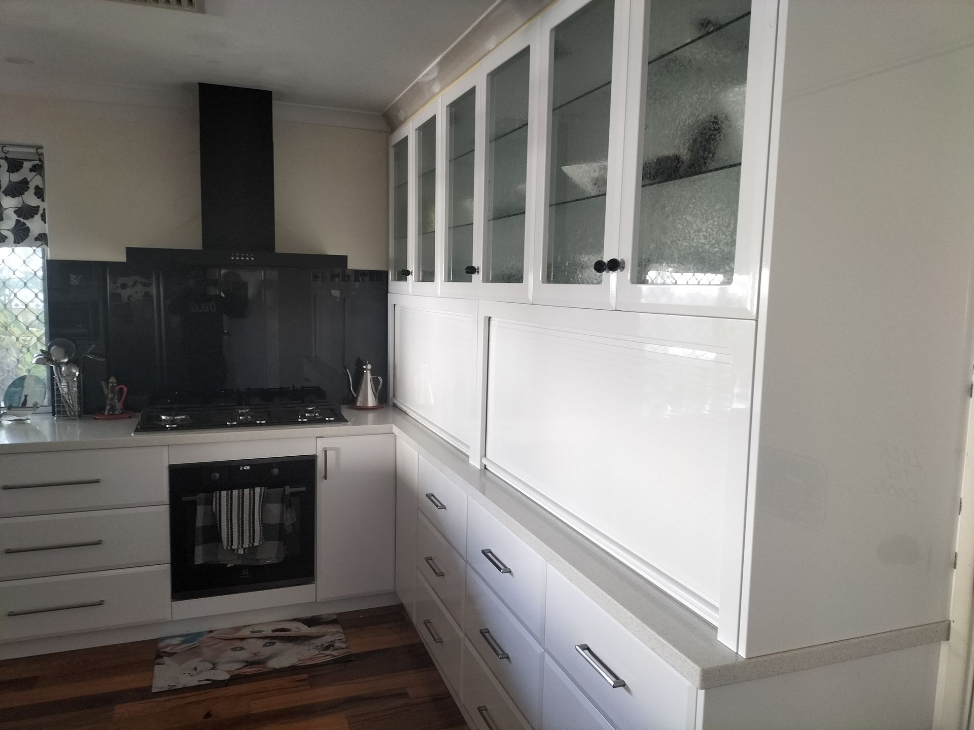 White kitchen with cabinets, stove, range hood, and glass-door upper cabinets.