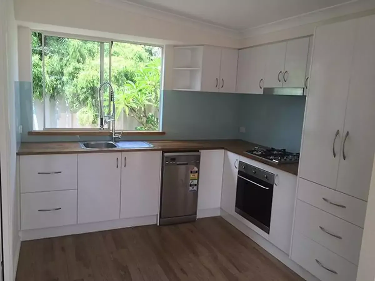 White kitchen with a window overlooking greenery, stainless steel appliances, and wooden countertops.