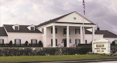 White funeral home with columns, flag, and sign reading 