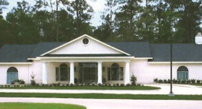 White building with columns, dark roof, arched windows, and a lawn.