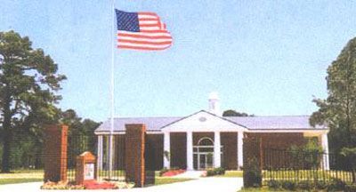 American flag waves above a brick building with white columns and a small cupola; two brick pillars are in the foreground.