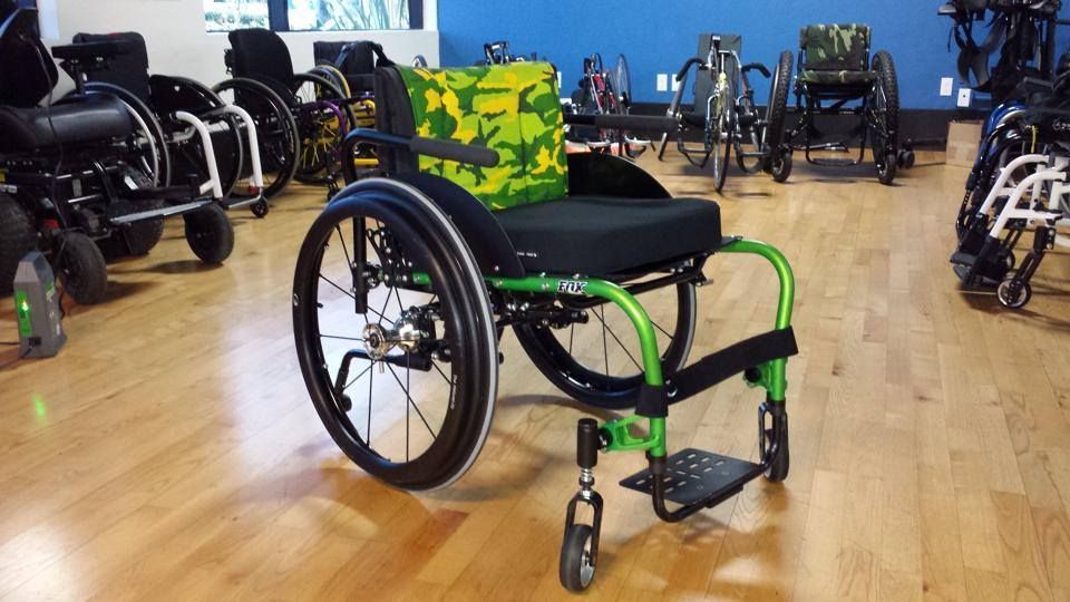 A green and black wheelchair is sitting on a wooden floor