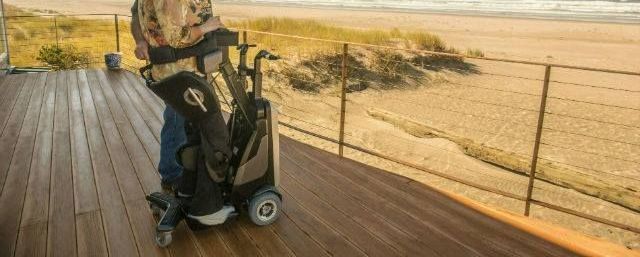 A person is pushing a golf bag on a scooter on a deck.