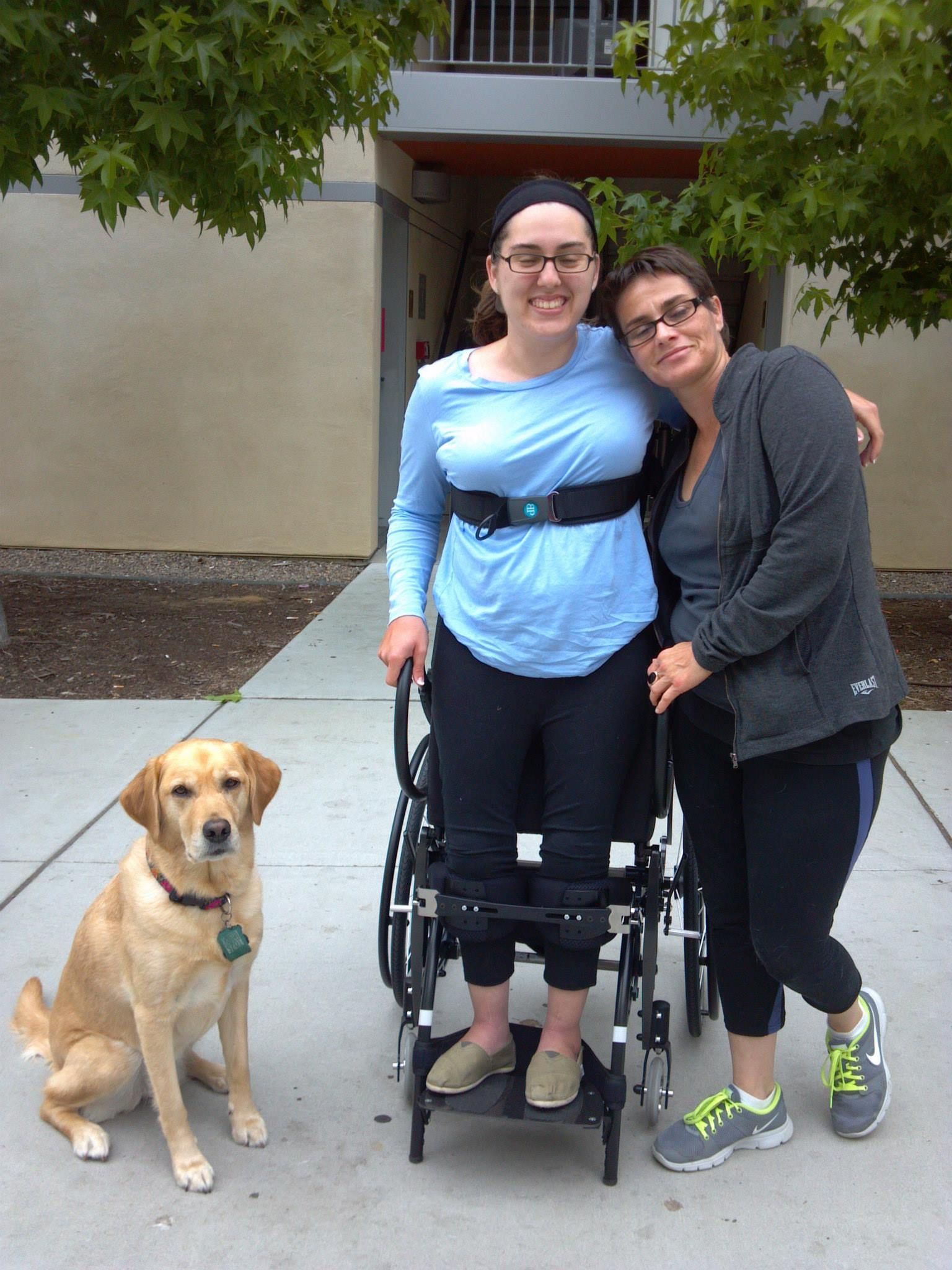 A woman in a wheelchair is standing next to two women and a dog