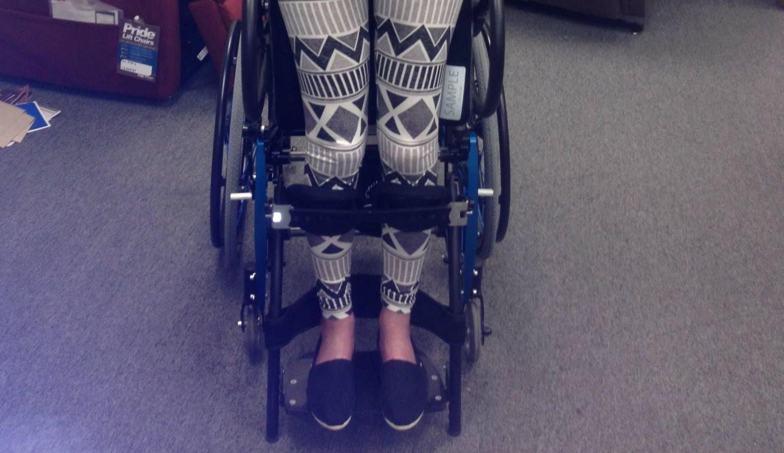 Person in a wheelchair, wearing patterned leggings and dark shoes, indoors.