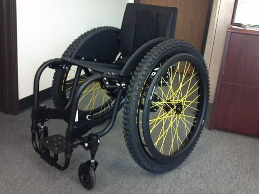 A black wheelchair with yellow wheels is sitting on the floor