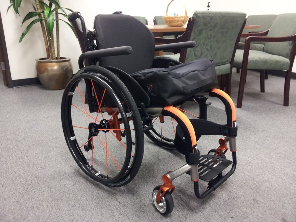 A black and orange wheelchair is in a room with chairs