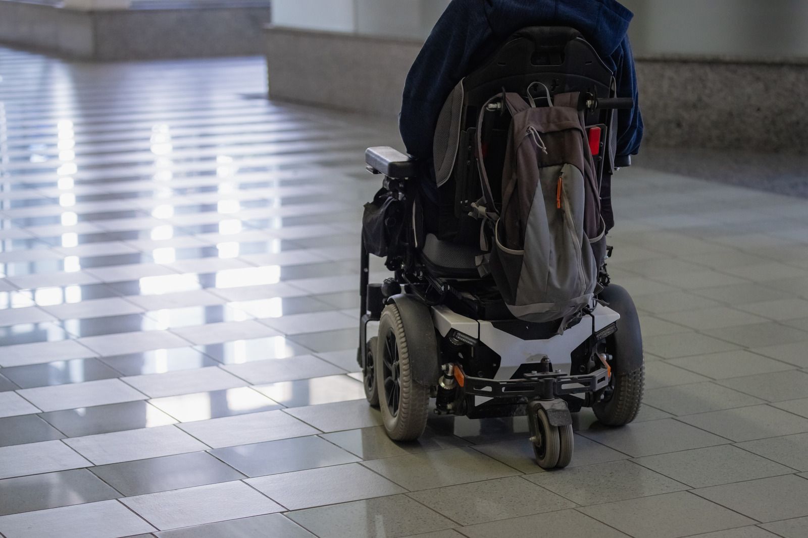 Empty wheelchair on a tiled indoor floor beside a bright window.