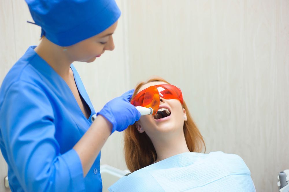 A woman is getting her teeth whitened by a dentist.