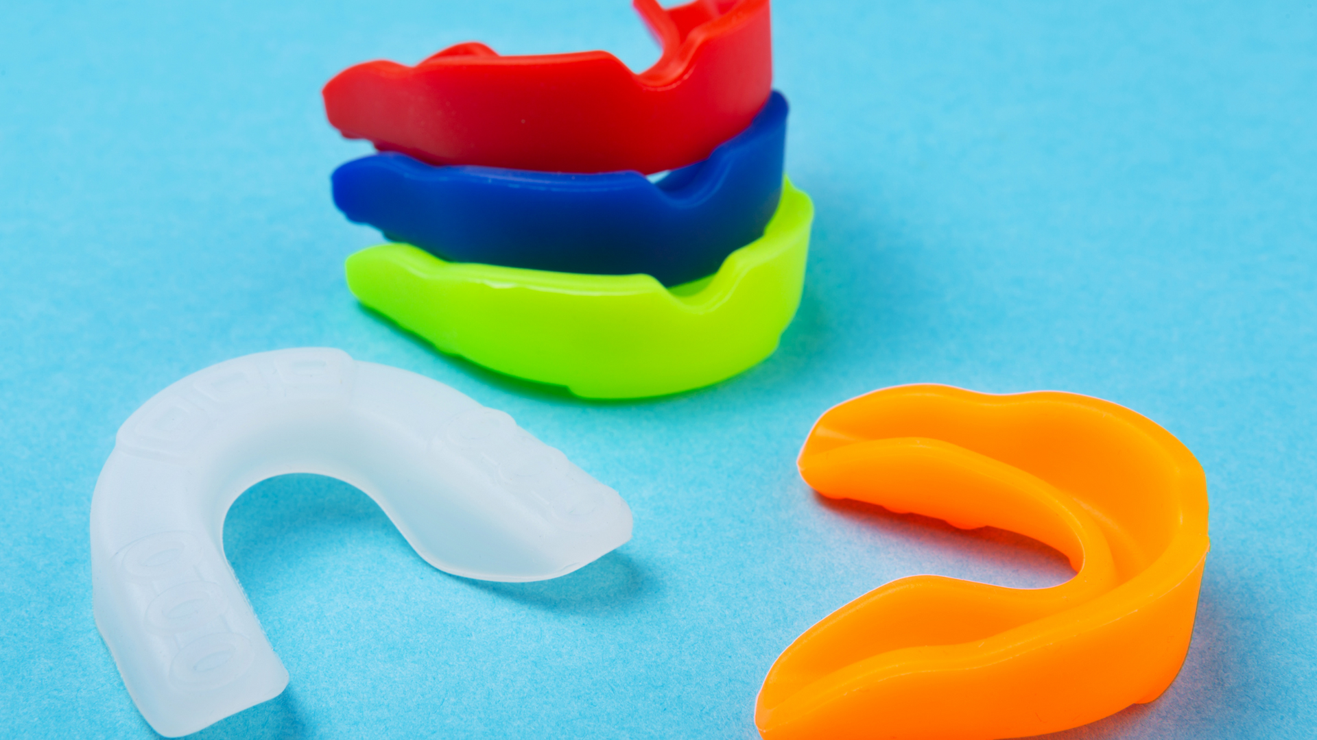 A group of mouth guards of different colors are stacked on top of each other on a blue surface.