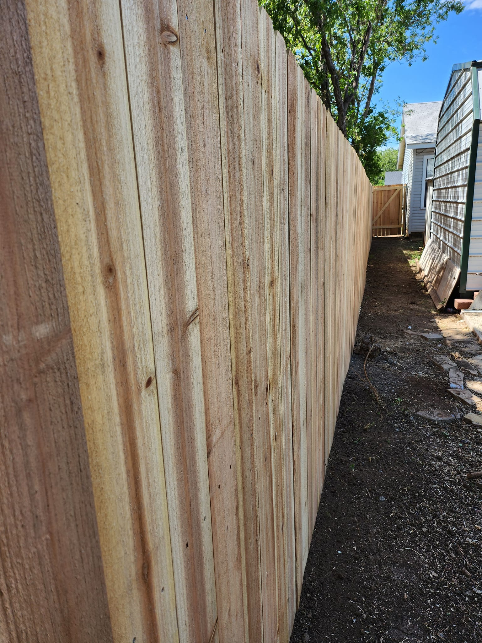 Wooden privacy fence, close-up, outdoors. Brown wood planks, gravel path. Sunlight.