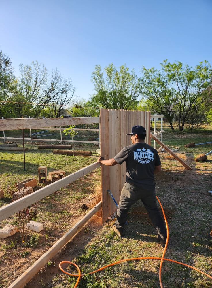 Person constructing a wooden fence in a sunny outdoor setting.