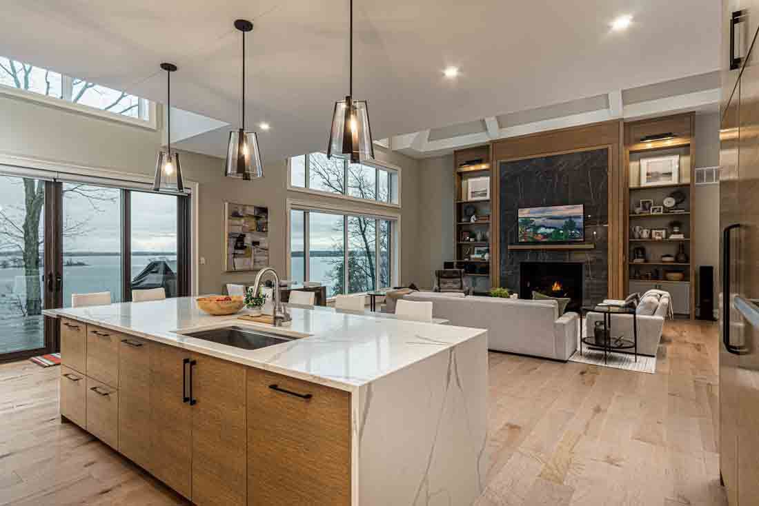 Modern open-concept kitchen with large island, wood cabinetry, white countertops, and floor-to-ceiling windows