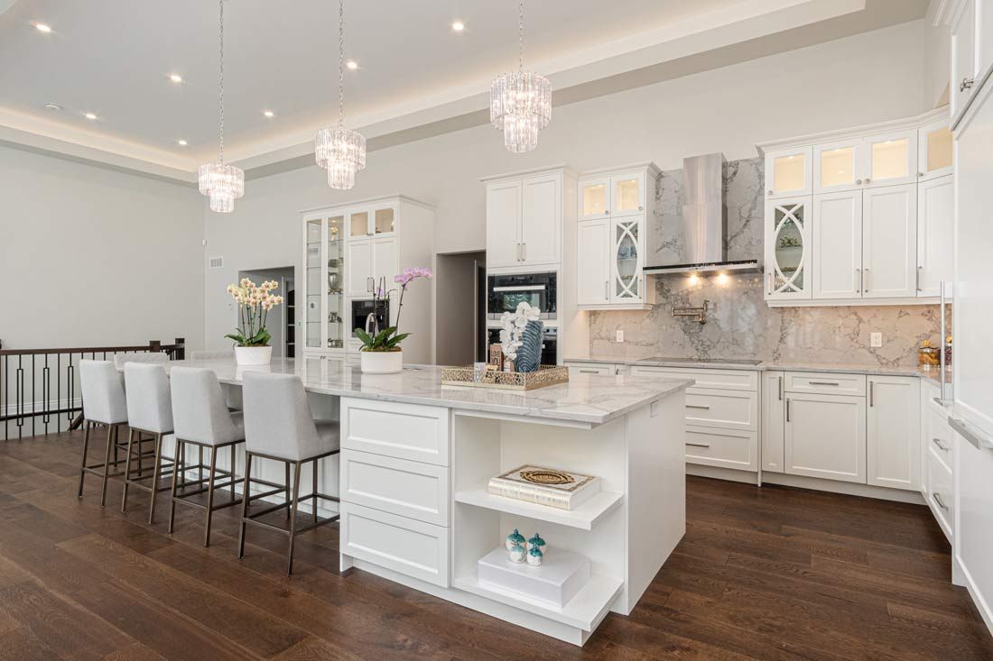 Bright white luxury kitchen with island, bar stools, chandeliers, and dark wood floors