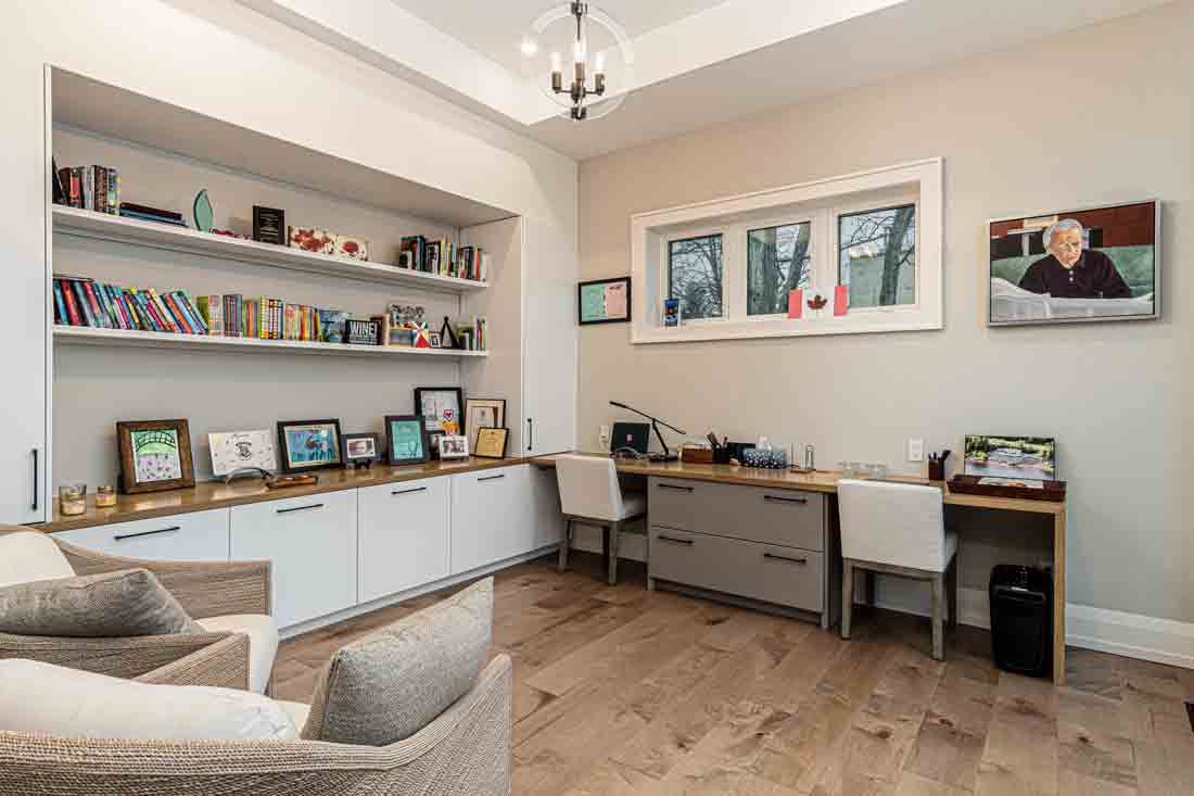 Bright home office with built-in shelves, desk, chair, framed photos, and an armchair on wood floors.