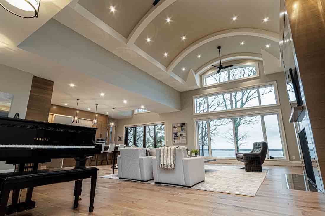 Bright modern living room with grand piano, white sofas, vaulted ceiling, and large windows