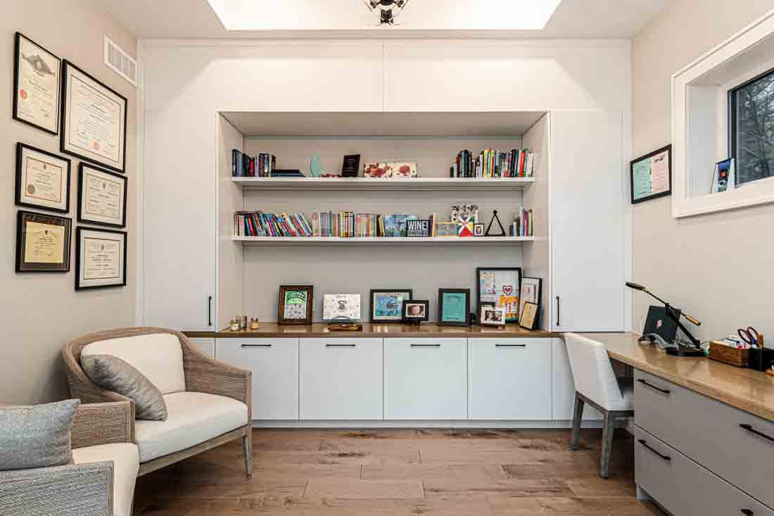 Bright home office with white built-in shelves, framed art, desk, chair, and beige armchair