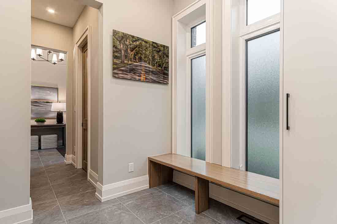 Modern hallway with gray tile floor, white walls, frosted windows, and a wooden bench by the entryway.