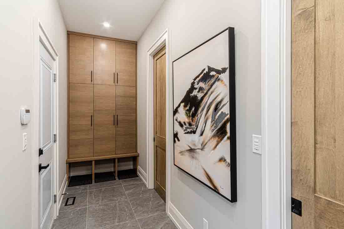 Narrow hallway with wood closets, white doors, and abstract wall art over gray tile floor