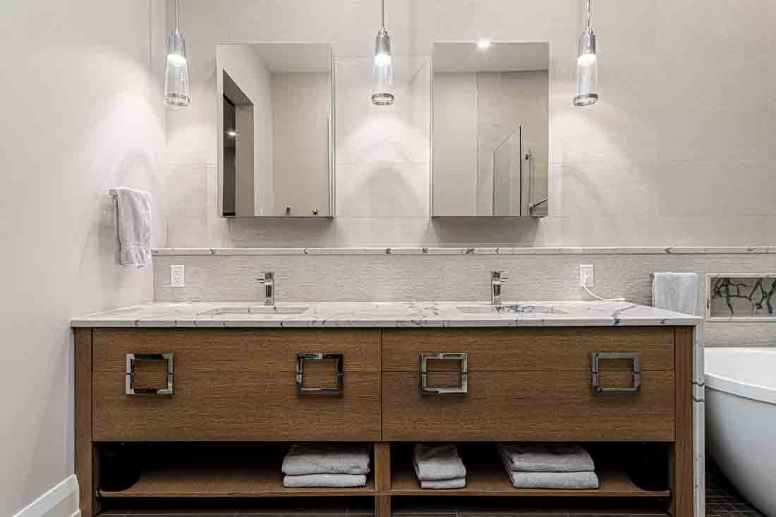 Modern bathroom with double sinks, mirrors, wall sconces, and a wooden vanity with towels underneath
