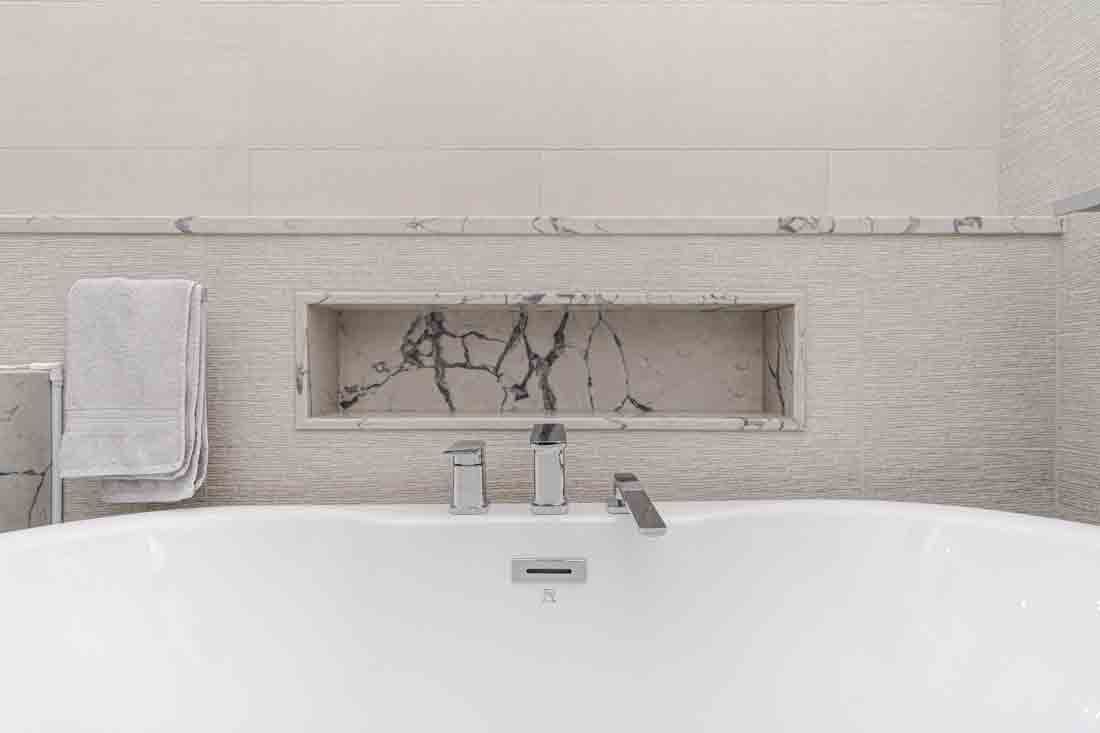 White bathroom with a freestanding tub, faucet, towel, and recessed shelf with branches and bottles.