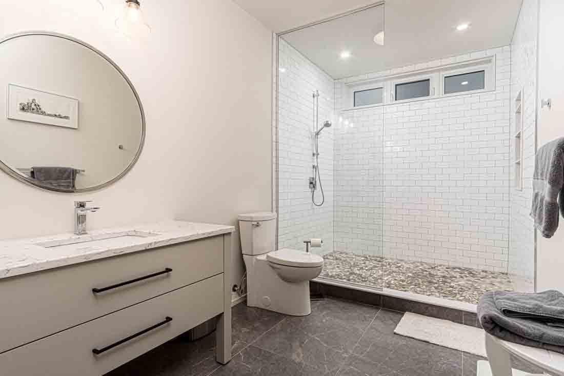 Modern white bathroom with walk-in shower, vanity, mirror, and gray tile floor