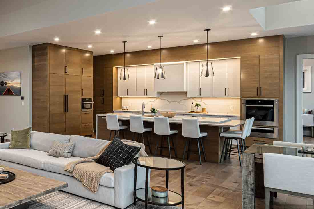 Modern open-plan kitchen and living room with a large island, white seating, and wood cabinetry